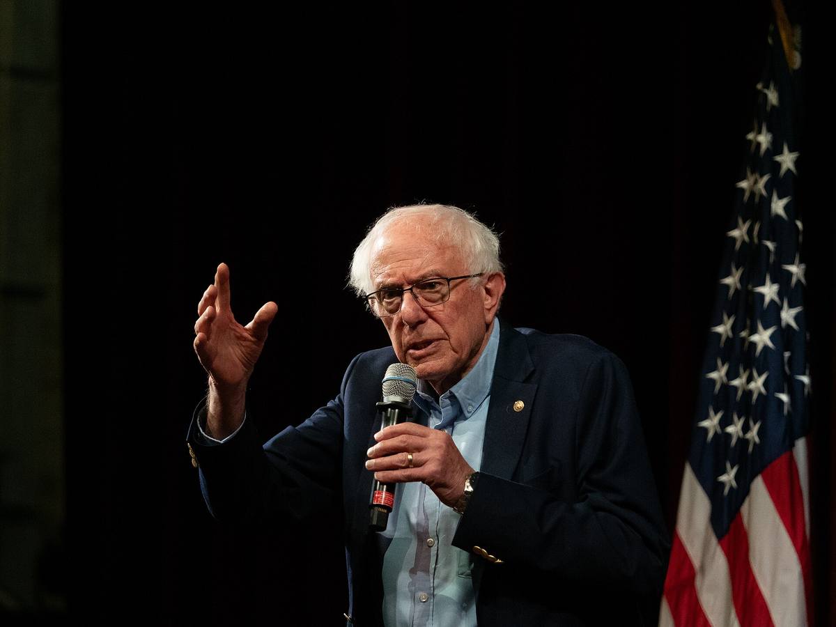 Bernie Sanders mluví do mikrofonu před americkou vlajkou