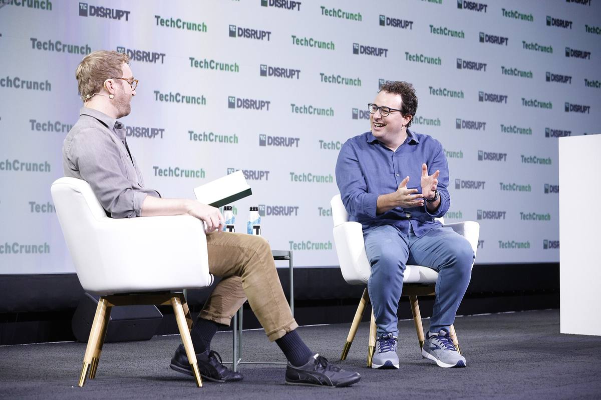Dario Amodei v modré košili sedí na pódiu konference TechCrunch Disrupt a gestikuluje