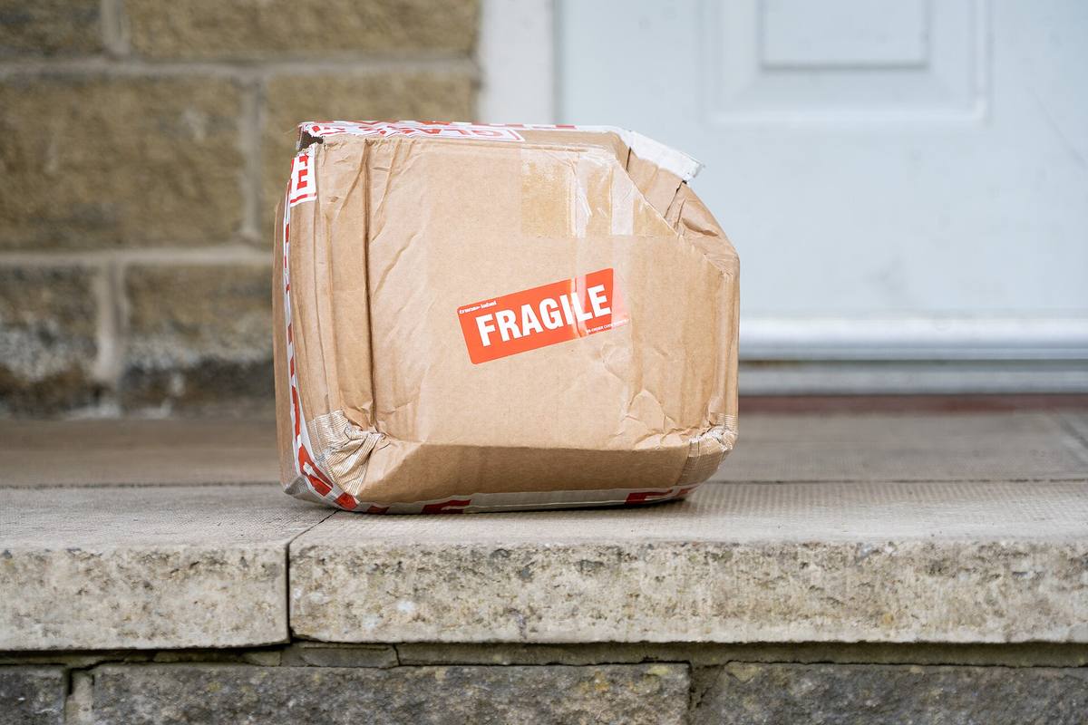 Pomačkaná kartonová zásilka se štítkem Fragile před dveřmi